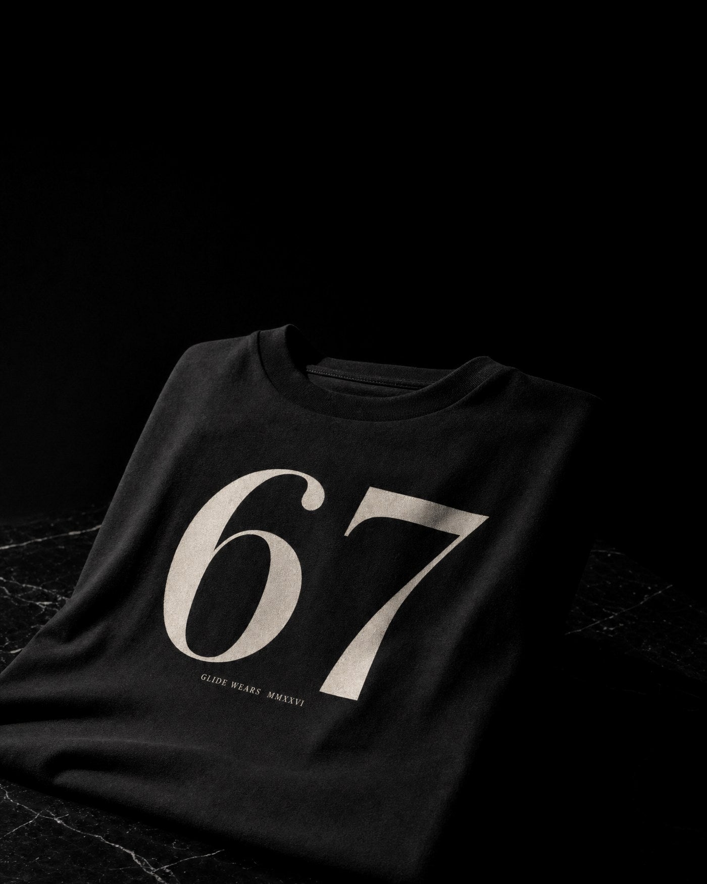 The Sixty-Seven Tee, folded obsidian cotton with cream Bodoni numerals.
